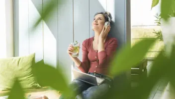 Smiling woman with headphones and laptop sitting outside drinking clean water.