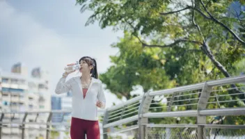 Asian woman drinking from reusable bottle while jogging outdoors hydrated exercise