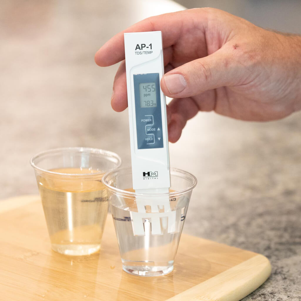 digital gauge measuring water levels in a clear glass of water compared to a dirty glass of water